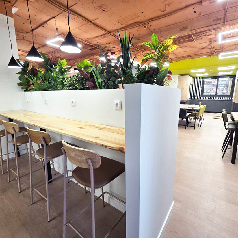 Área de coworking con barra de trabajo, taburetes altos y separación vegetal para mayor privacidad.