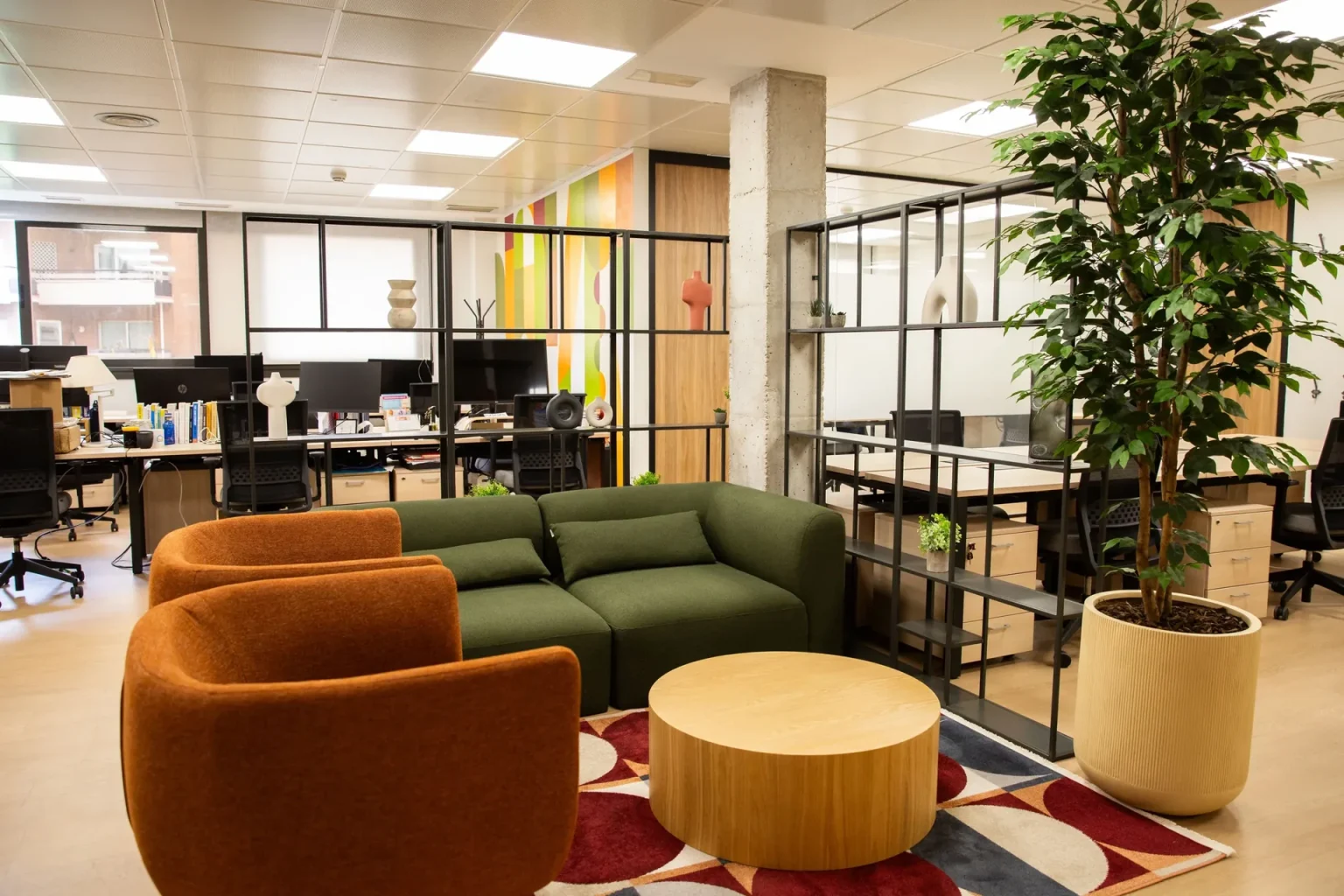 Zona de descanso con sillones naranjas y un sofá verde, y puestos de trabajo al fondo